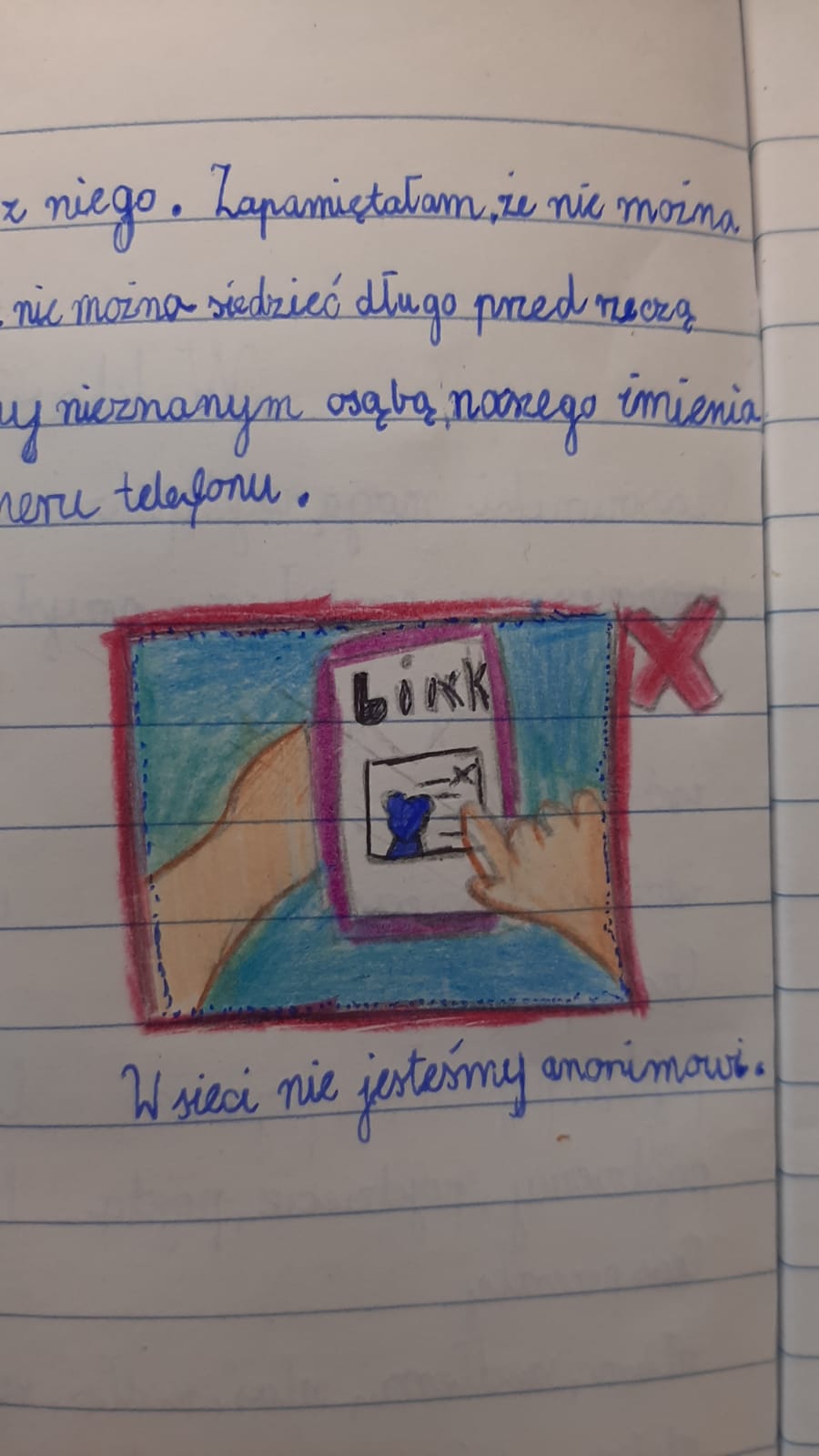 Zbliżenie na stronę w zeszycie ucznia. Widnieje tam odręczny tekst w języku polskim dotyczący zasad bezpieczeństwa (m.in. o niepodawaniu imienia i numeru telefonu nieznajomym) oraz kolorowy rysunek przedstawiający smartfon z napisem „Link” i czerwonym krzyżykiem obok. Pod rysunkiem napis: „W sieci nie jesteśmy anonimowi”.