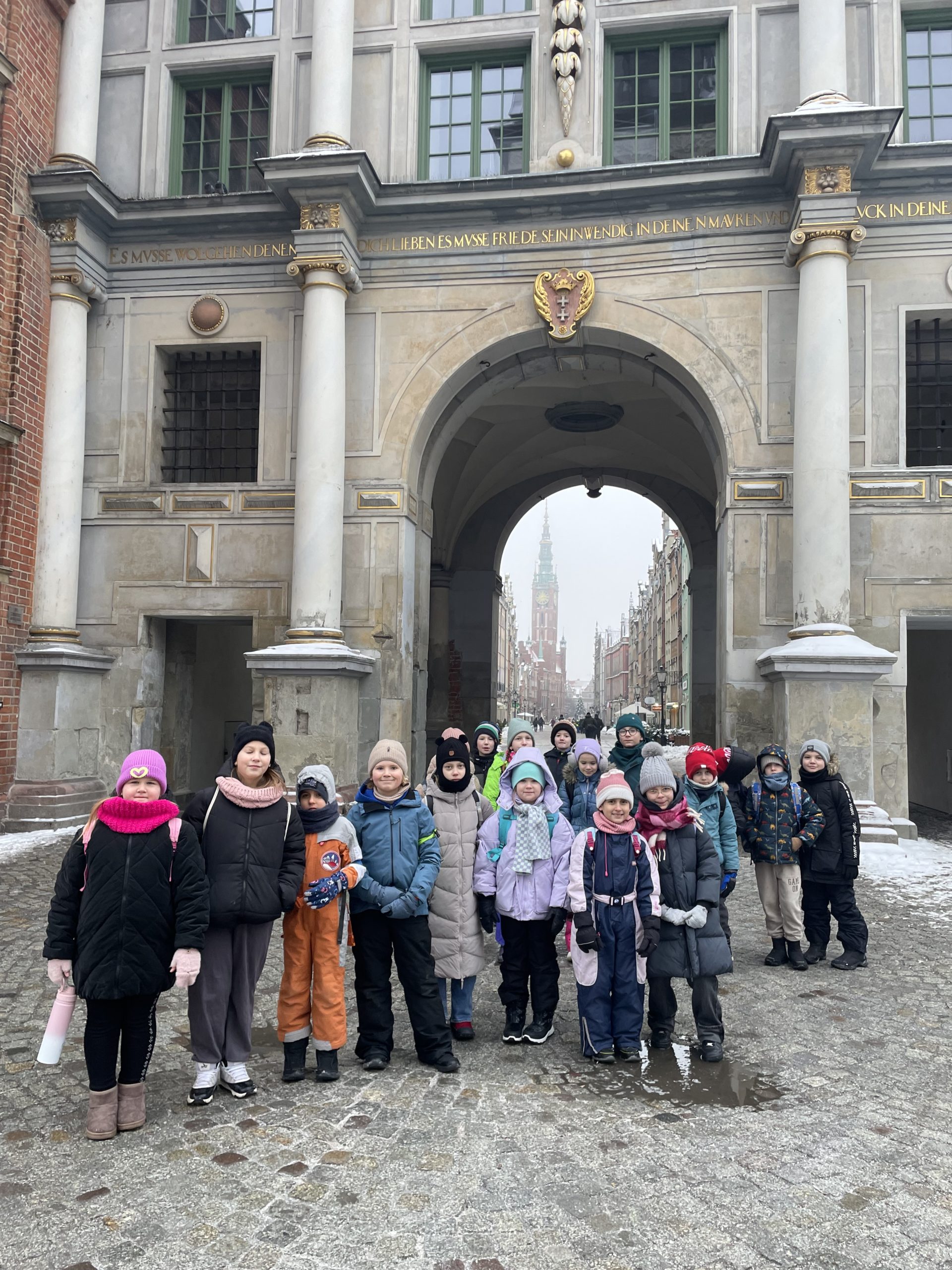 Grupa dzieci stoi przed Złotą Bramą w Gdańsku.