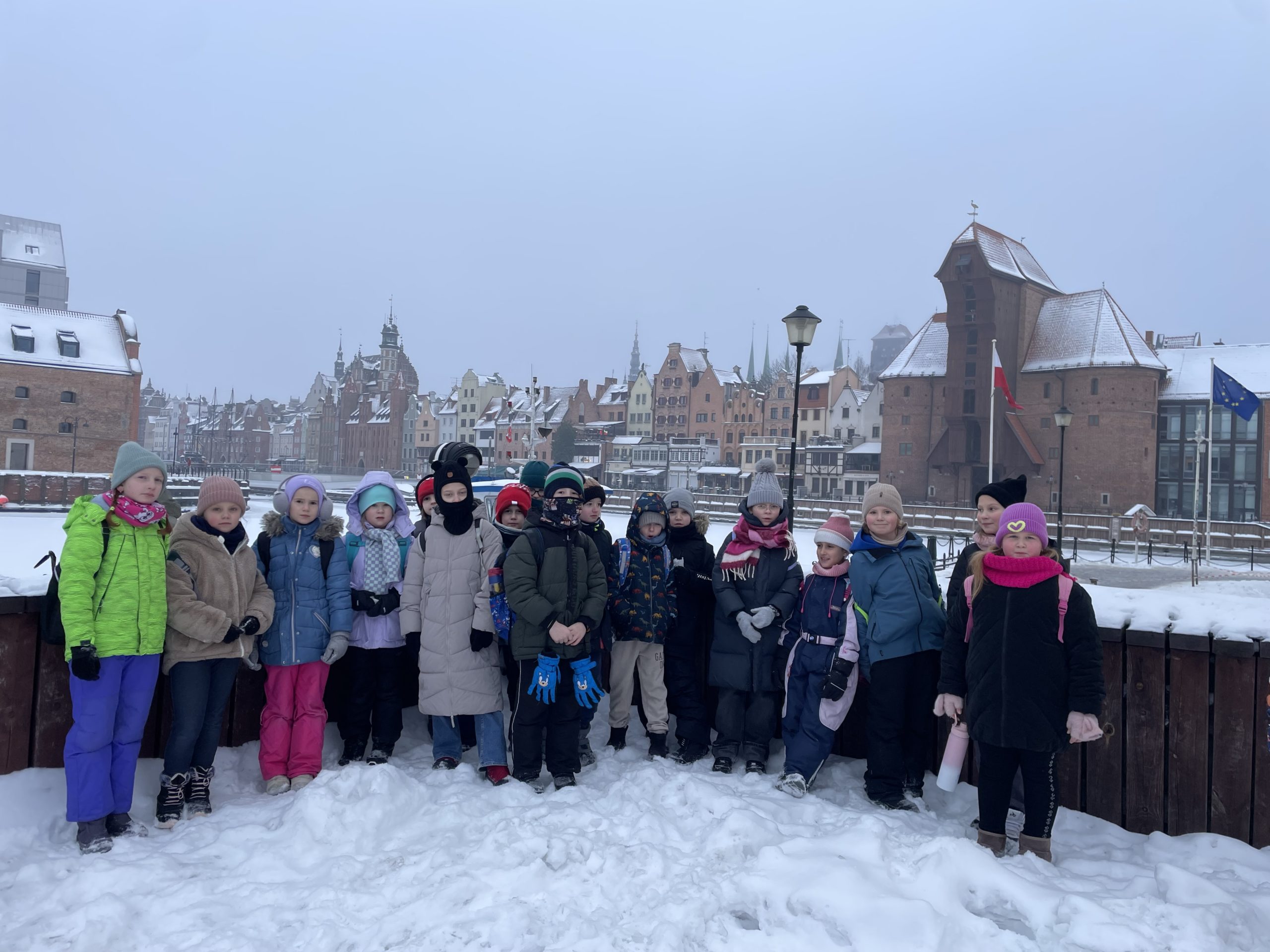 17 uczniów stoi na tle zamarzniętej Motławy i Żurawia.