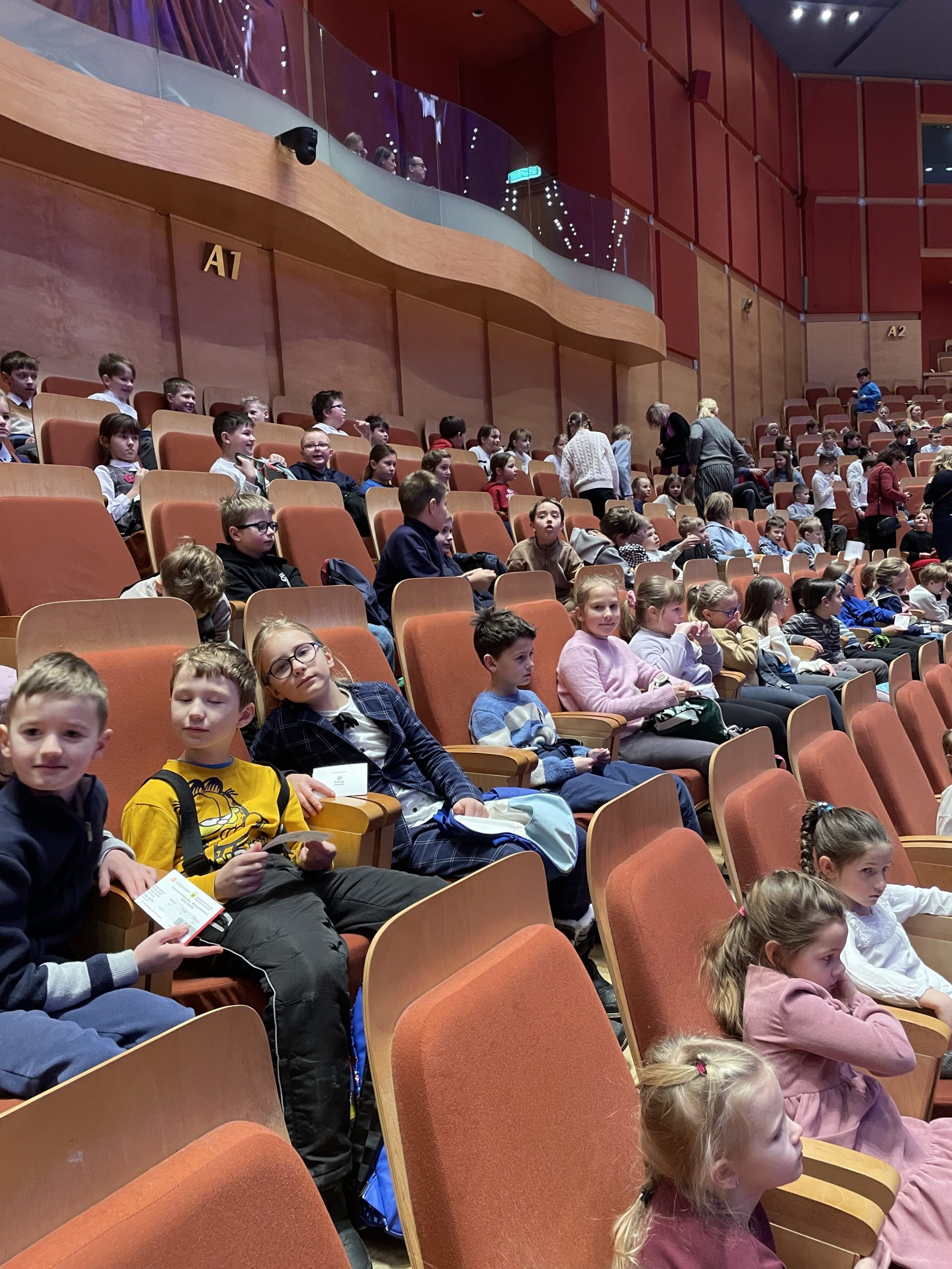 .Dzieci siedzą w fotelach w sali Filharmonii Bałtyckiej.