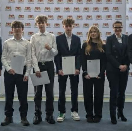 Grupa uczniów wraz z p. prezydent Gdańska stoi przed ścianką z herbem Gdańska. Każdy z uczniów trzyma dyplom potwierdzający otrzymanie stypendium.