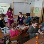 Na tle tablicy multimedialnej z napisem DZIĘKUJĘ ZA SPOTKANIE koło stolika ze sprzę-tem medycznym stoi kobieta z kroplówką w rękach. Obok niej przyglądające się dzieci.