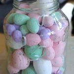 Słoik wypełniony pastelowymi jajkami.