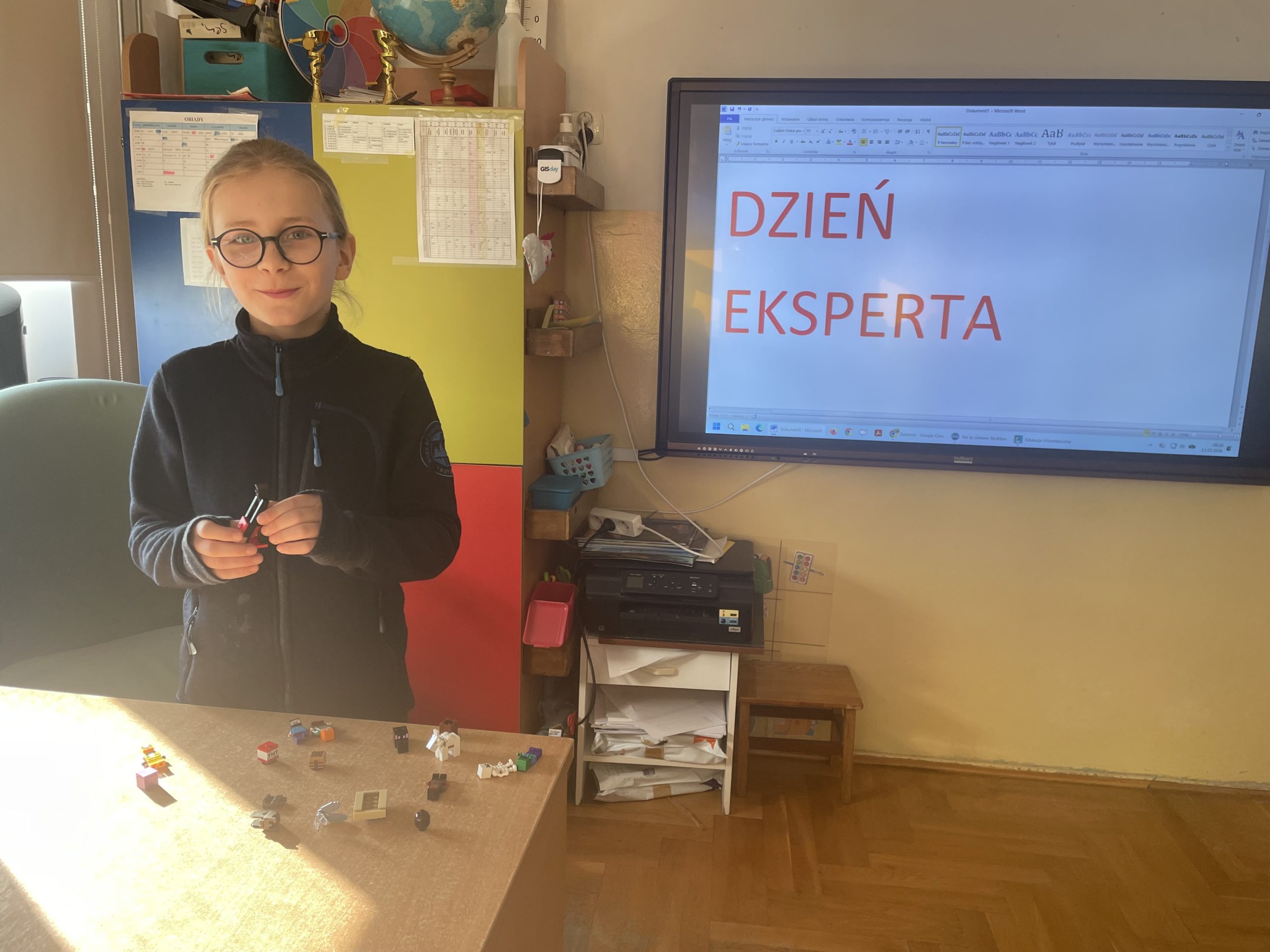 Chłopiec stoi przed biurkiem na którym leżą figurki z klocków Lego.