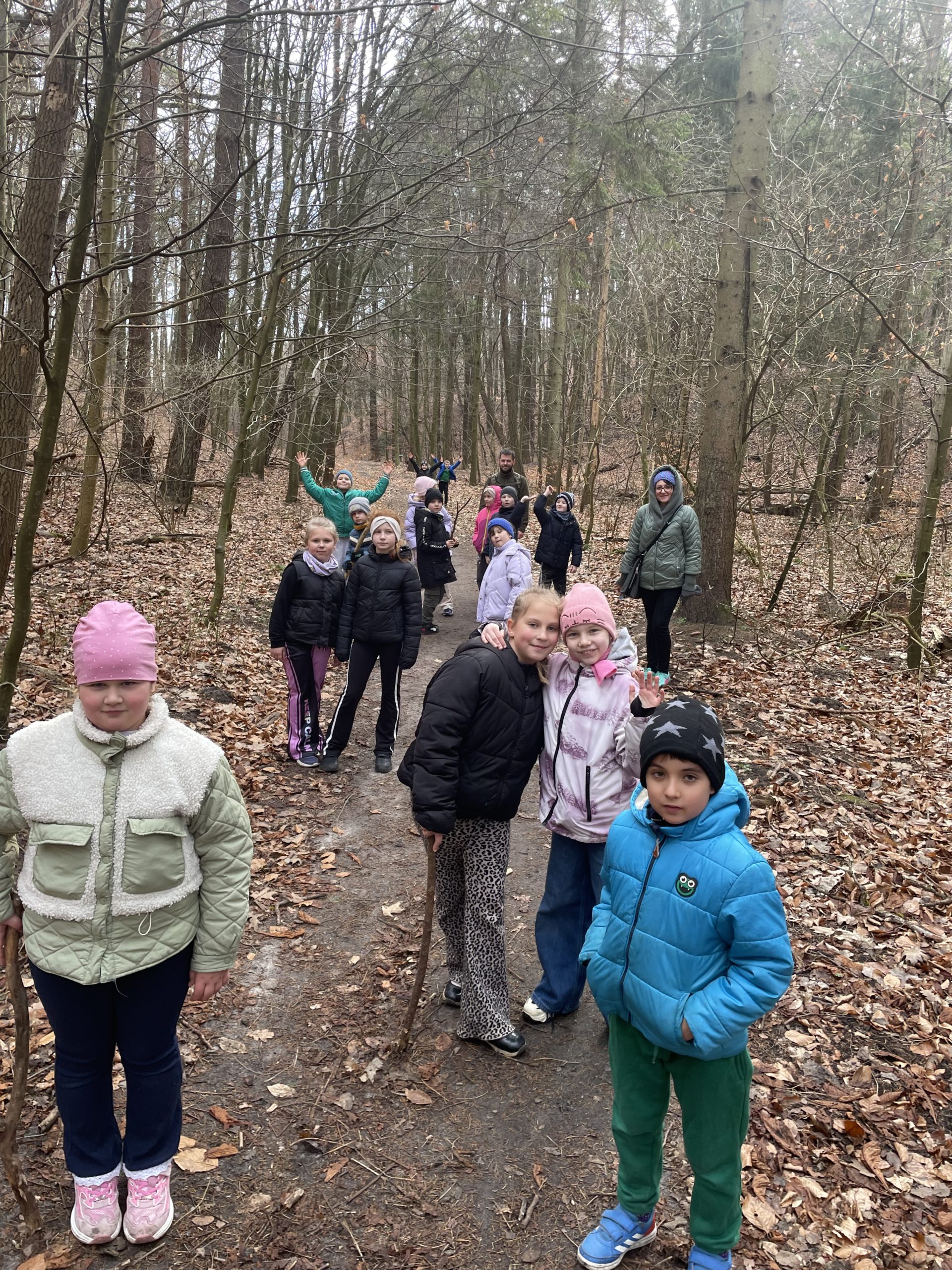 Grupa kilkunastu uczniów idzie ścieżką w lesie.
