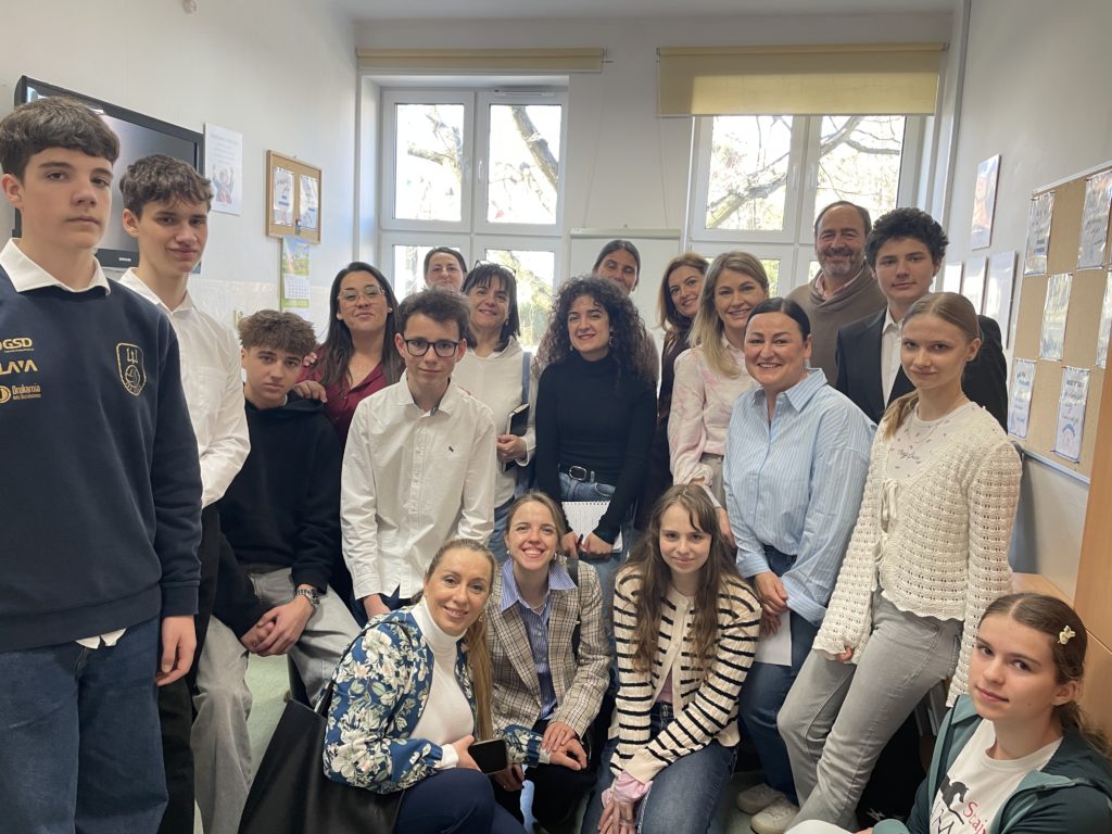 Grupa ok 15 osób (uczniowie i osoby dorosłe) pozuje do zdjęcia. W tle widać dwa okna