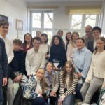 Grupa ok 15 osób (uczniowie i osoby dorosłe) pozuje do zdjęcia. W tle widać dwa okna