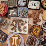 Stół pełen domowych wypieków ozdobionych symbolem liczby pi – ciasta, muffiny i ciasteczka z kolorowymi dekoracjami oraz cyframi rozwinięcia π.