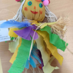 Kolorowa, ręcznie wykonana lalka z żółtą twarzą, włosami ze sznurka i strojem z bibuły oraz piór.