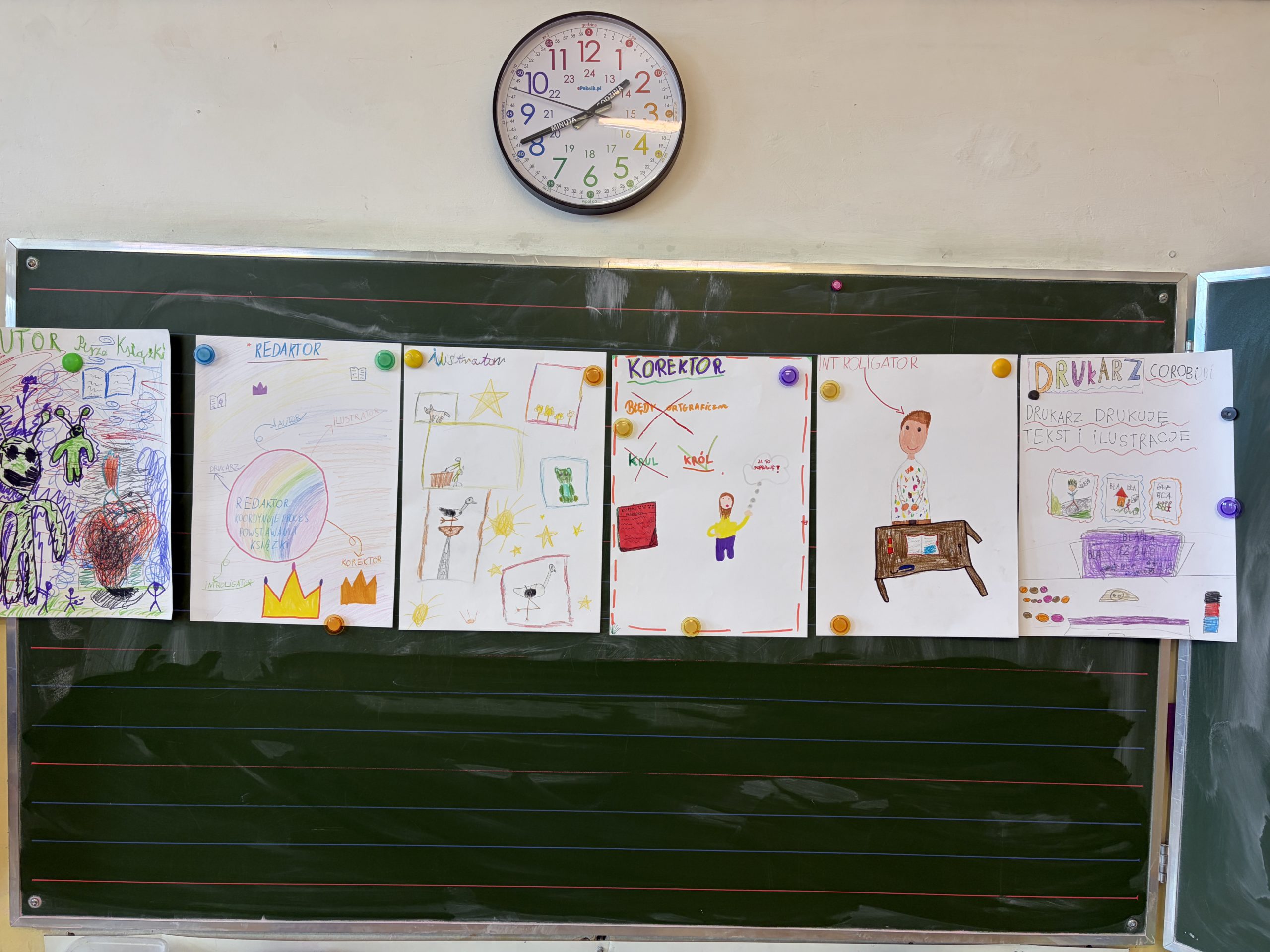 Seria sześciu kolorowych, dziecięcych plakatów przypiętych magnesami do szkolnej tablicy, ilustrujących zawody związane z powstawaniem książki, takie jak autor, redaktor czy drukarz. Nad tablicą wisi zegar ścienny.