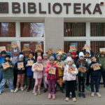 Na tle budynku z napisem BIBLIOTEKA stoi grupa uczniów klasy 1c z indeksami Akademii Gdańskich Lwiątek w dłoniach.