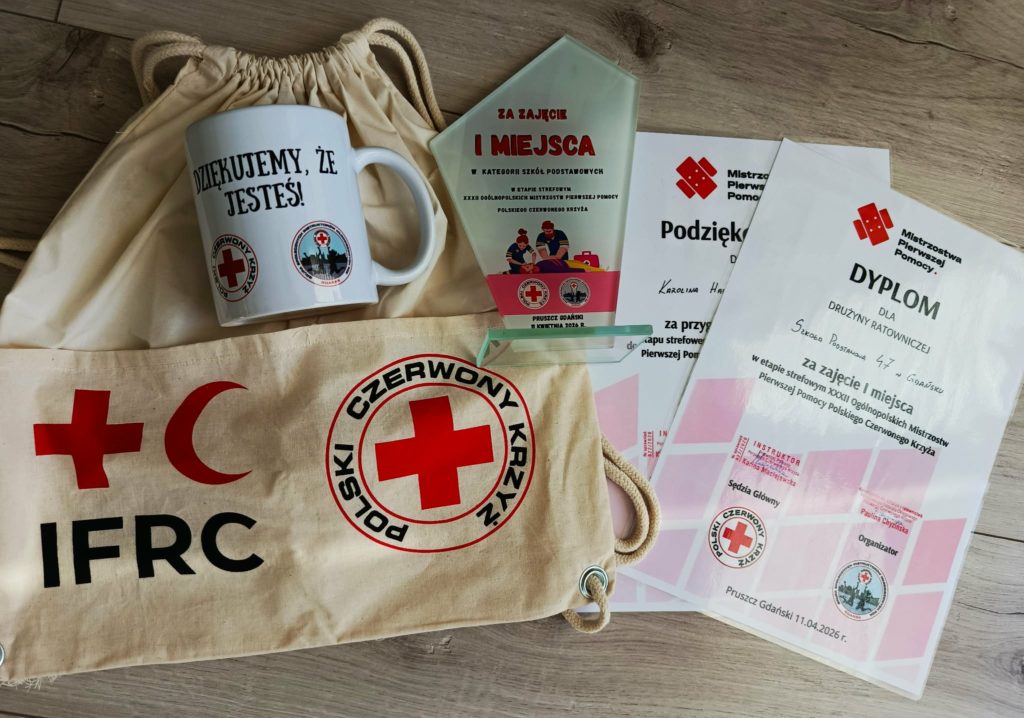 Na podłodze leżą: statuetka i dyplomy za zajęcie I miejsca w etapie rejonowym XXXII Ogólnopolskich Mistrzostw Pierwszej Pomocy PCK oraz kubek i worek z logiem PCK.