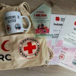 Na podłodze leżą: statuetka i dyplomy za zajęcie I miejsca w etapie rejonowym XXXII Ogólnopolskich Mistrzostw Pierwszej Pomocy PCK oraz kubek i worek z logiem PCK.