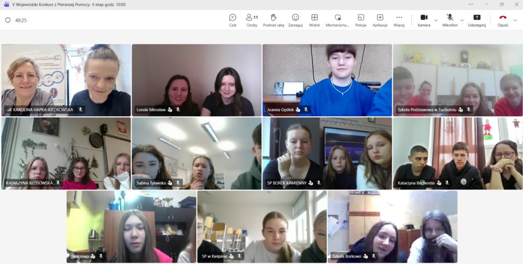 Na jasnym tle okna aplikacji Teams widok z 11 kamer. W każdym okienku przed komputerem siedzi drużyna składająca się trzech zawodników. W lewym górnym rogu organizatorka konkursu na tle plakatu „NAJWIECEJ POMOCY JEST W PIERWSZEJ POMOCY”.