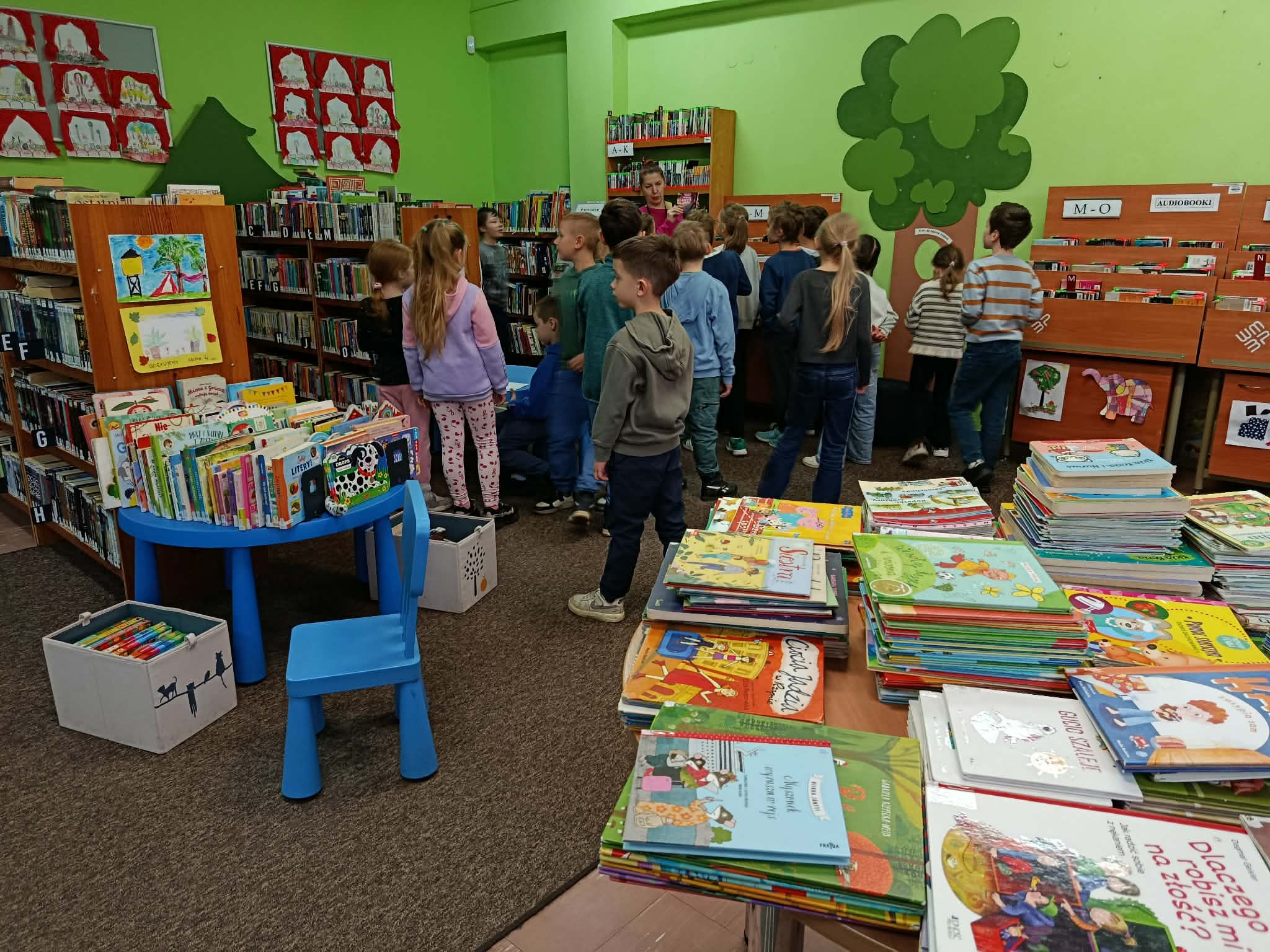 W wypożyczalni na tle regałów z książkami dla dzieci grupa uczniów klasy 1c wraz z bibliotekarką.