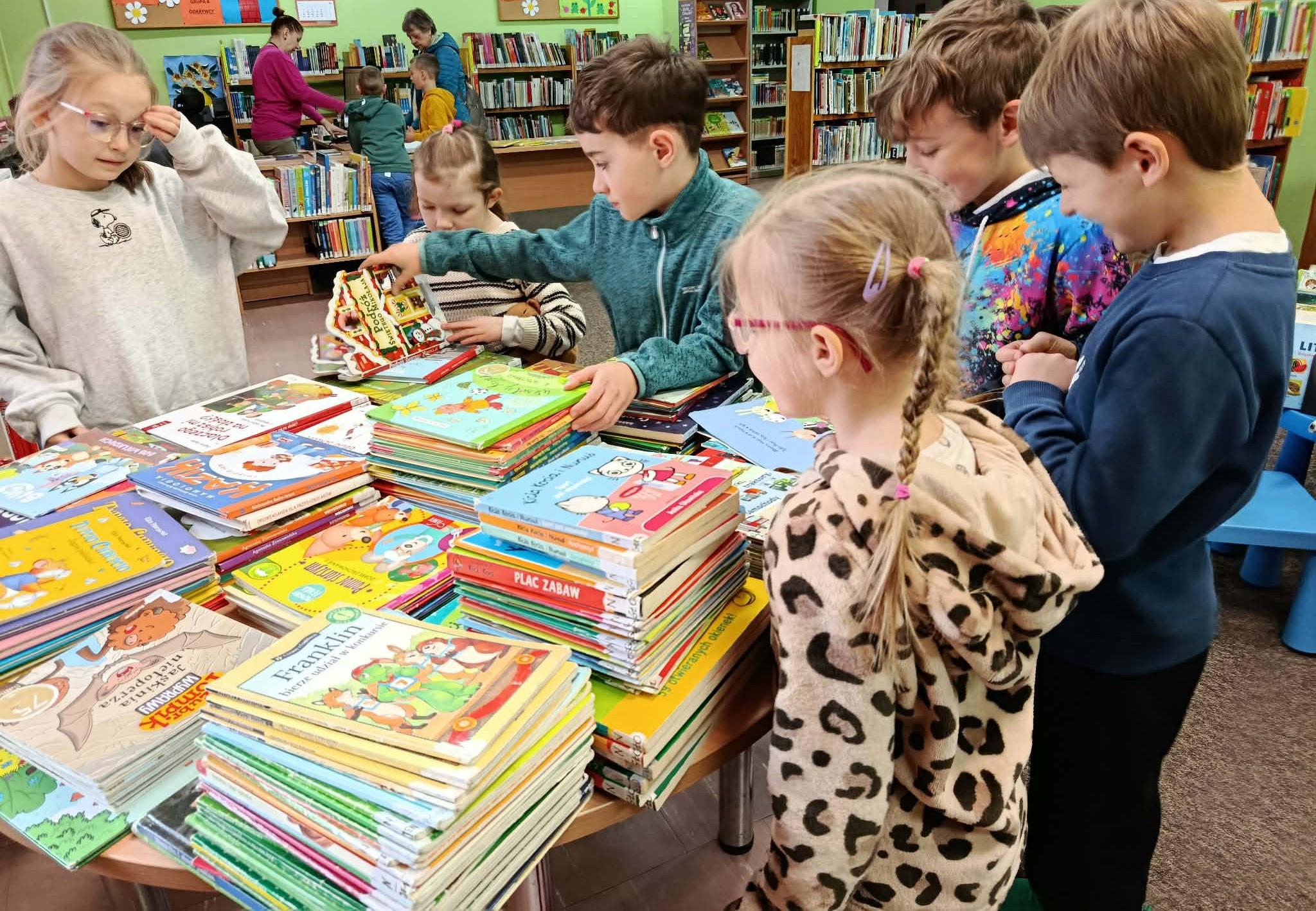 Przy stole z książkami sześcioro uczniów klasy 1c, w tle regały z książkami i stanowisko do wypożyczania.