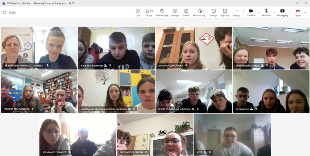 Na jasnym tle okna aplikacji Teams widok z 11 kamer. W każdym okienku przed komputerem siedzi drużyna składająca się trzech zawodników. W lewym górnym rogu organizatorka konkursu na tle plakatu „NAJWIECEJ POMOCY JEST W PIERWSZEJ POMOCY”.