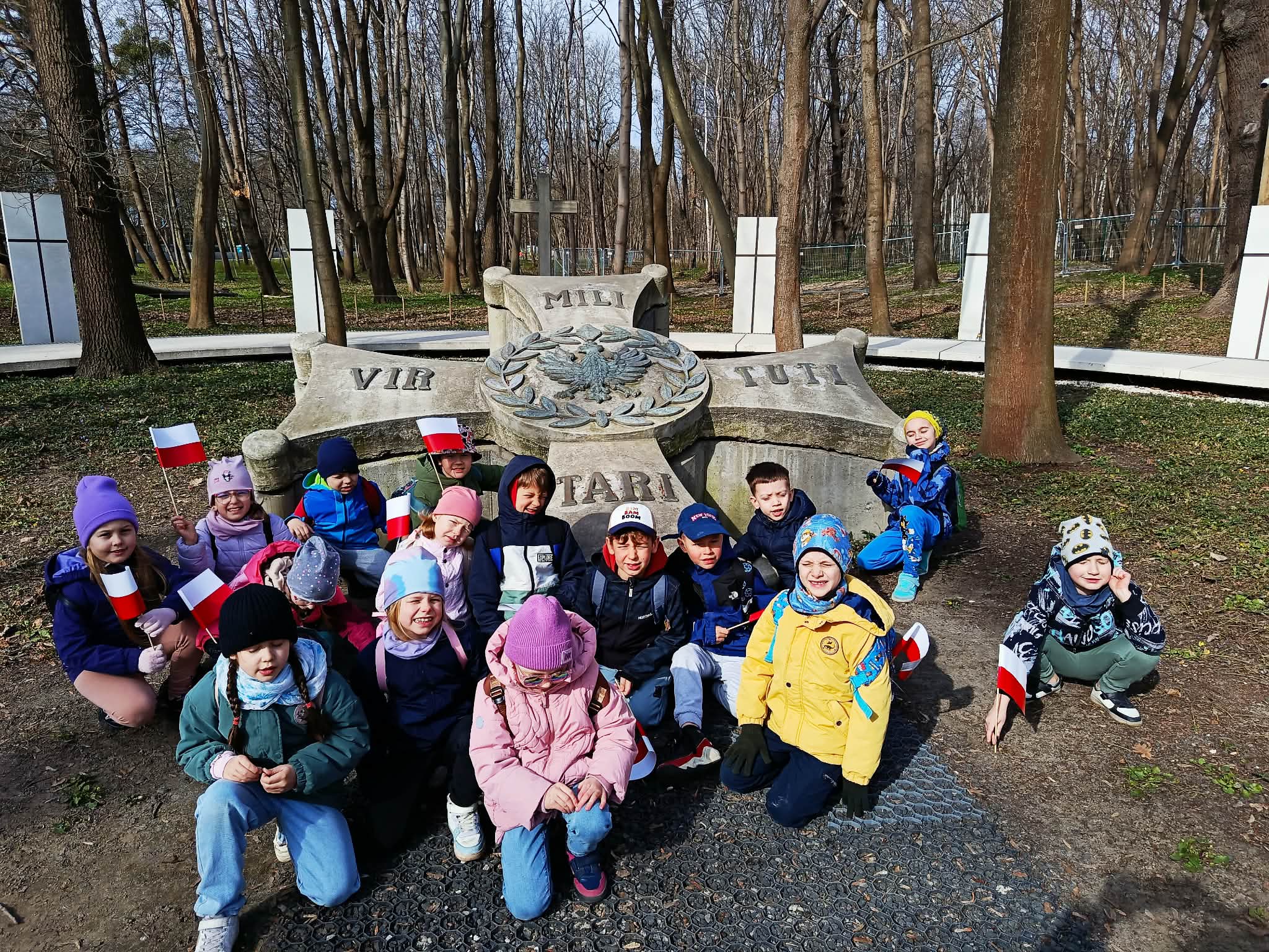 Grupa uczniów kucająca przed pomnikiem na Cmentarzu Poległych Obrońców Wester-platte.