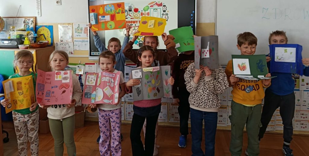 Na tle tablic grupa uczniów trzymających w rękach lapbooki promujące zdrowy tryb życia.