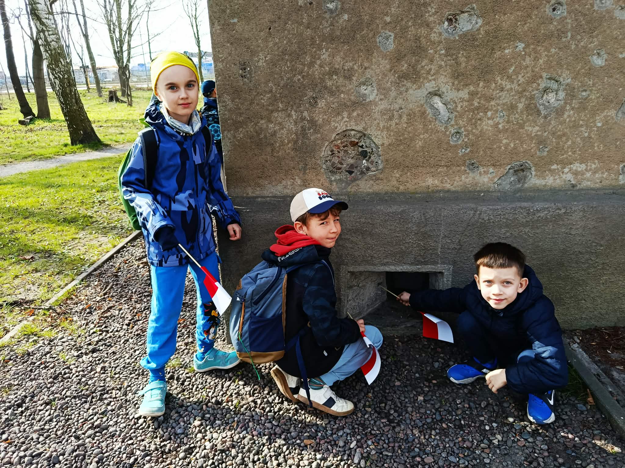 Trzech uczniów wskazujących okienko strzelnicze w Wartowni nr 1 na Westerplatte.