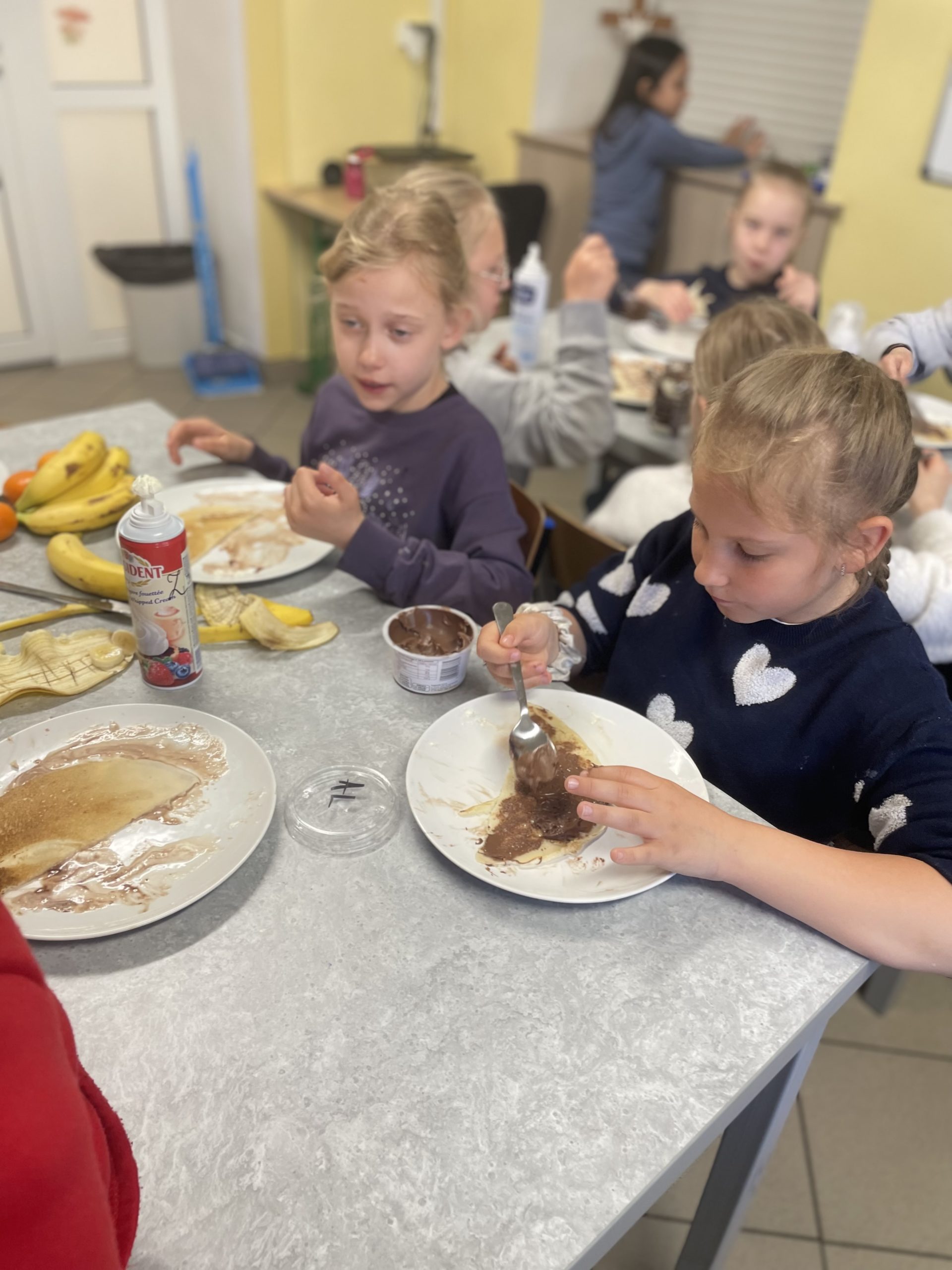 Kilkoro dzieci siedzą przy stole i jedzą naleśniki.