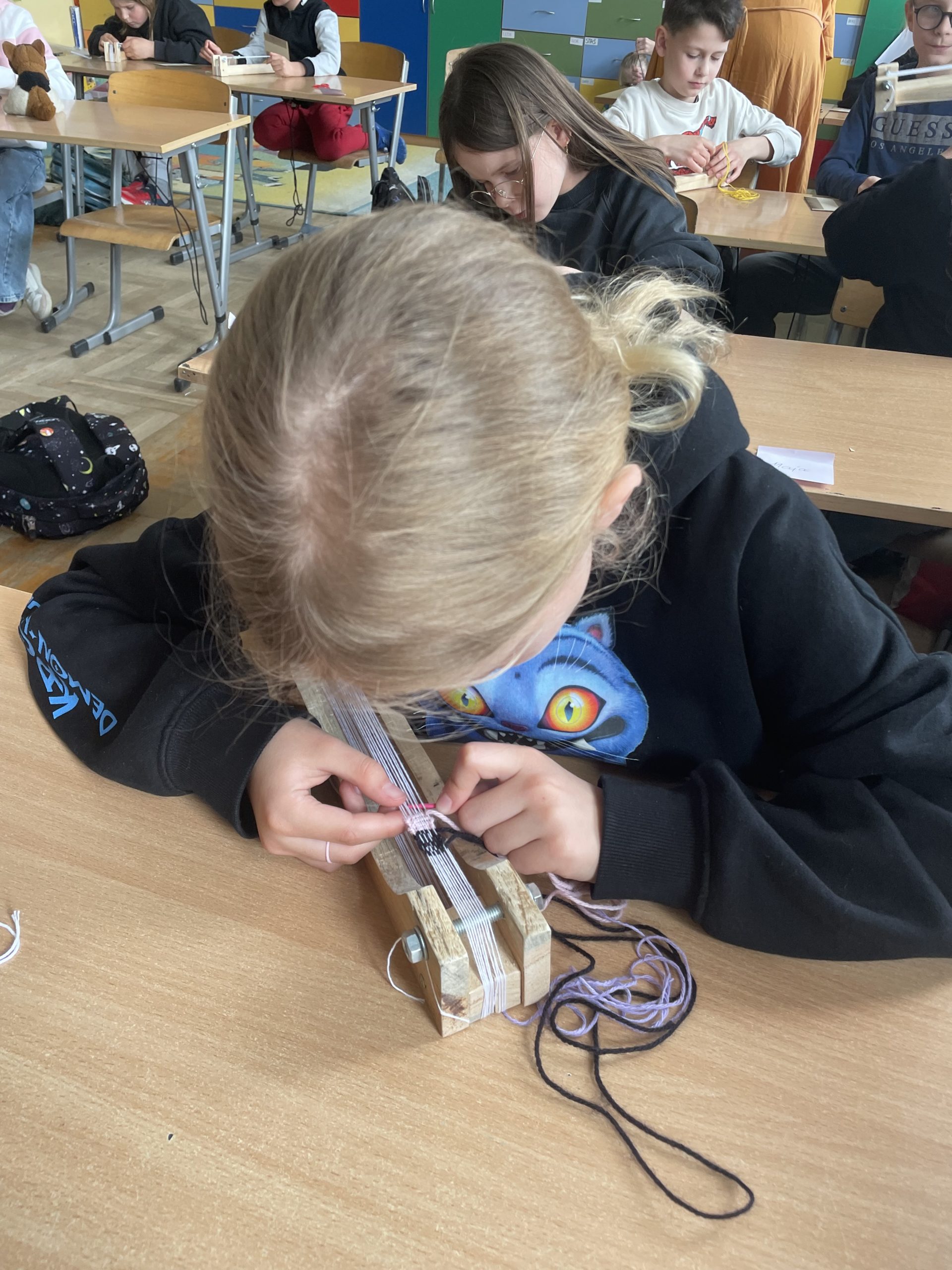 dziewczynka siedzi przy stole, jest nachylona nad małym krosnem