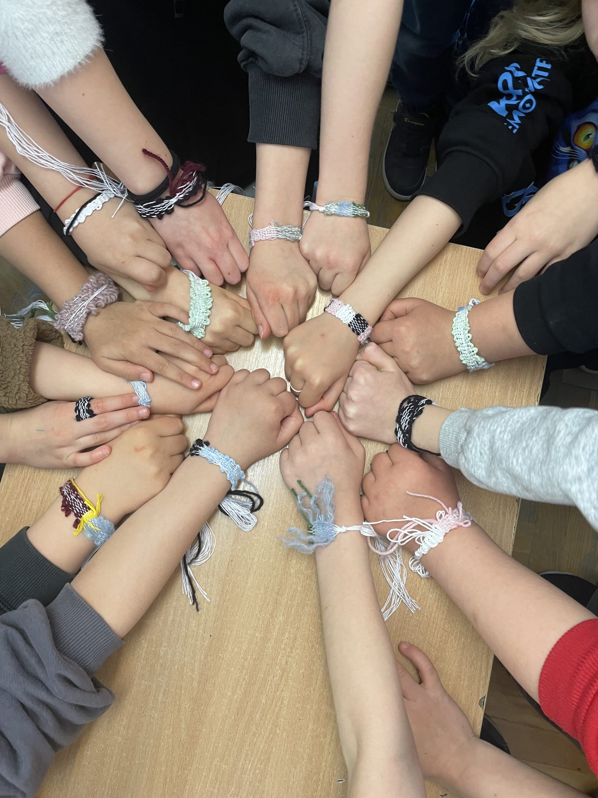 14 rąk ułożonych w kółko prezentuje bransoletki.