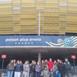 Grupa uczniów – wolontariuszy stoi przed wejściem do hali Polsat Plus Arena w Gdańsku. Ubrani w kurtki i bluzy, pozują wspólnie do zdjęcia na tle charakterystycznej elewacji budynku.