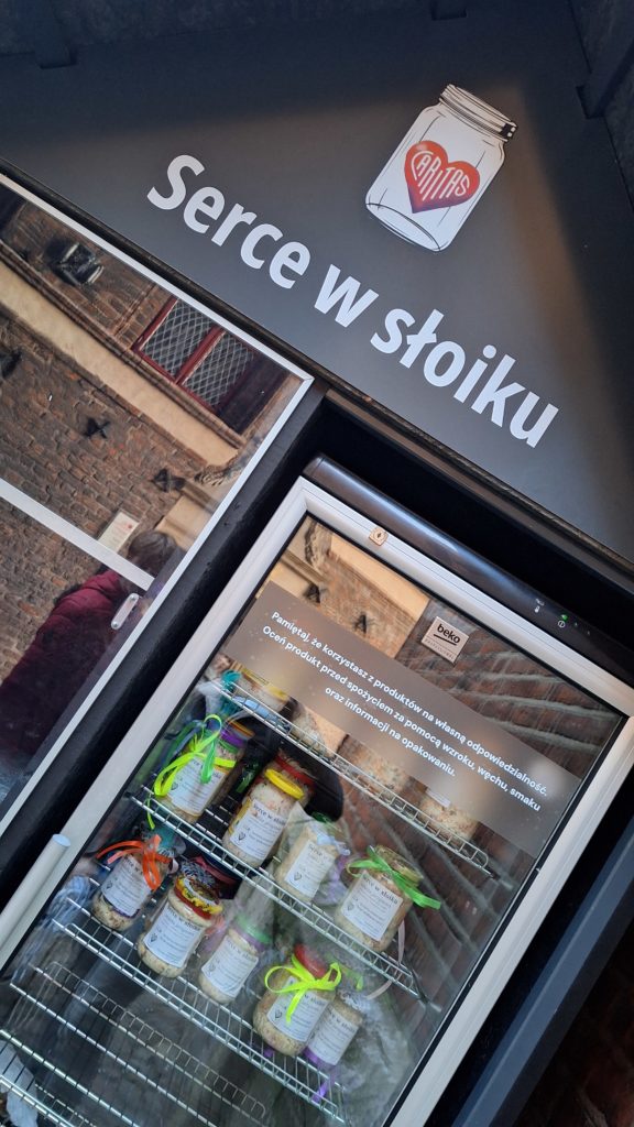 Lodówka z napisem „Serce w słoiku” i rysunkiem słoika z sercem. W lodówce stoją słoiki z przygotowanym jedzeniem, ozdobione wstążkami. 