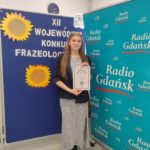 Tosia Flasińska stoi na tle dekoracji konkursowych i prezentuje swój dyplom.