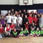W sali gimnastycznej na tle banerów stoi ustawiona w kilka rzędów około pięćdziesięcioosobowa grupa ludzi: ratowników GUMed, uczniów, opiekunów drużyn i organizatorów konkursu z pierwszej pomocy. Trzy drużyny trzymają puchary.