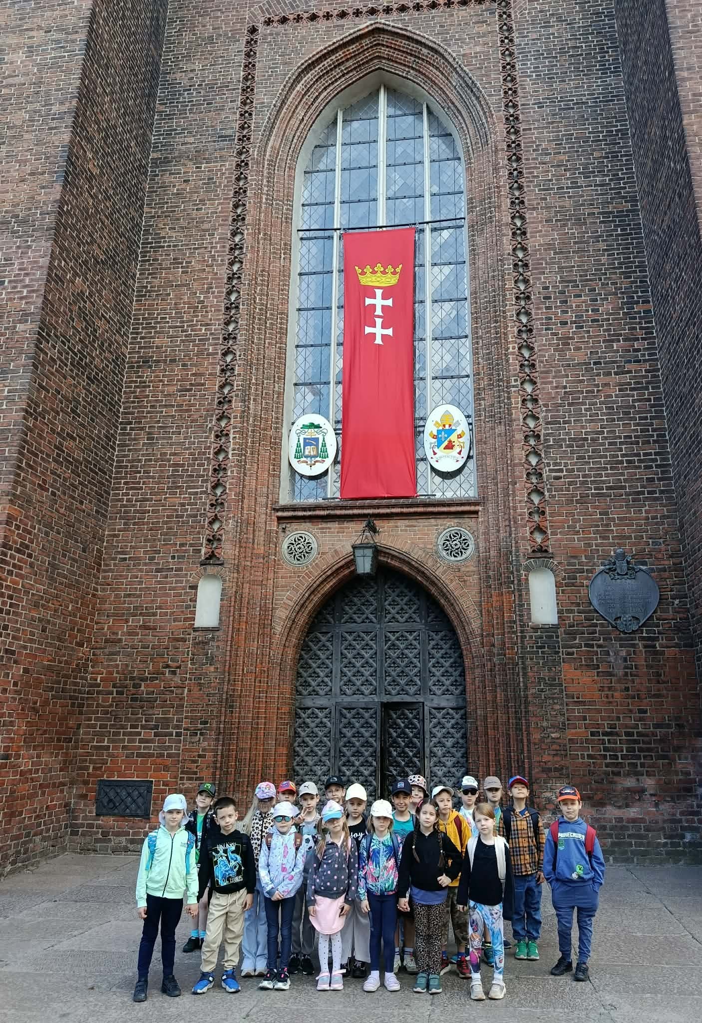 Na tle wejścia głównego do Bazyliki Mariackiej z rozwieszoną nad nim flagą Gdańska stoi klasa 1c i pozuje do zdjęcia.