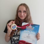 Uczennica prezentuje medal Mistrzyni Polski oraz dyplom za I miejsce w cheerleadingu sportowym.