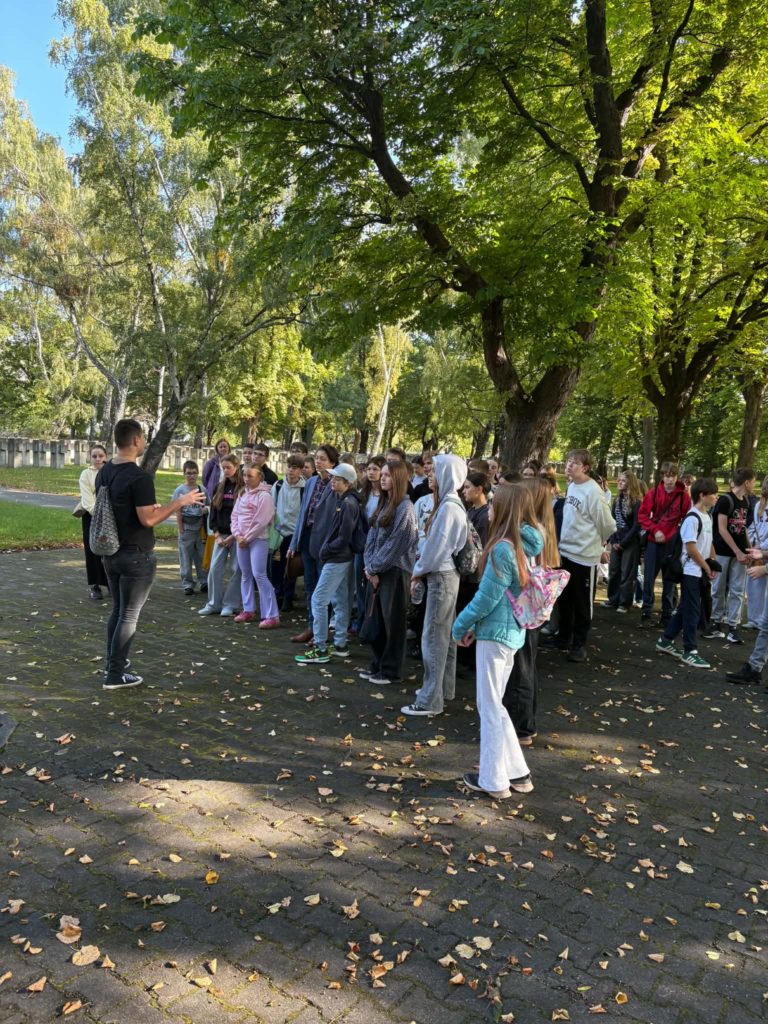 Grupa uczniów stojących na cmentarzu na tle drzew podczas lekcji historii w terenie