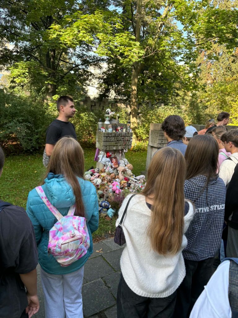 Grupa uczniów i nauczyciel historii stają przed Pomnikiem na cmentarzu na Zaspie
