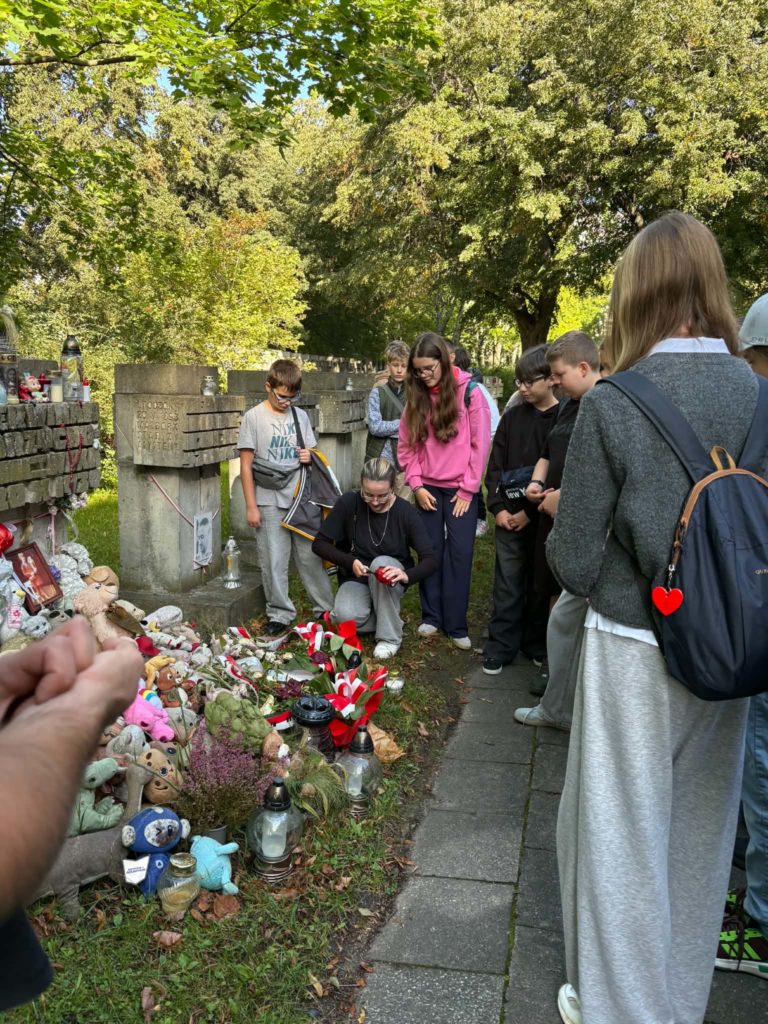 Grupa młodzieży szkolnej, która zapala znicze w miejscu pamięci narodowej -cmentarz na Zaspie