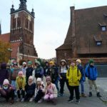 Na tle zabytkowego młyna i kościoła świętej Katarzyny stoją uczniowie klasy 2c ustawieni w dwóch rzędach i pozujący do zdjęcia.