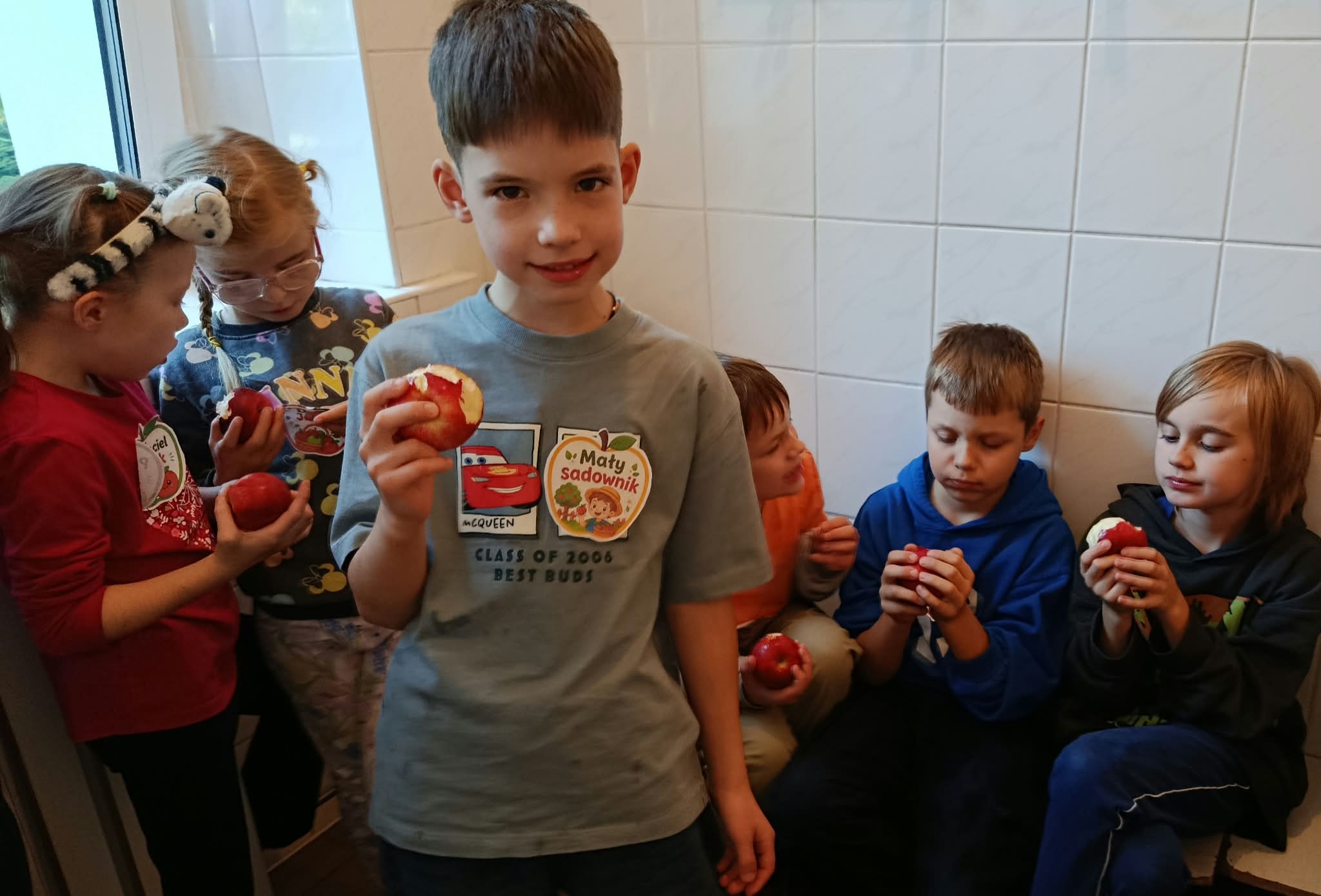 Na pierwszym planie uczeń klasy 2c trzymający w ręku nagryzione jabłko. W tle 5 innych uczniów tej klasy z jabłuszkami w rękach.