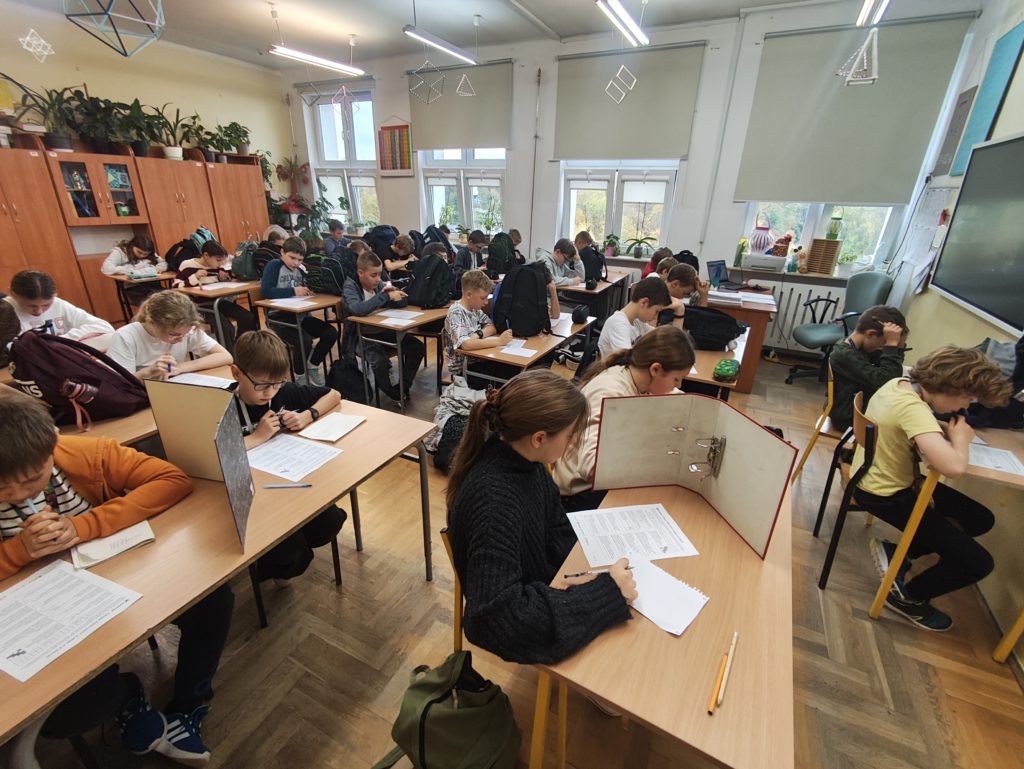 W sali matematycznej siedzą uczniowie w ławkach i są pochyleni nas pisaniem pracy pisemnej. Uczniowie są skupieni i zamyśleni.