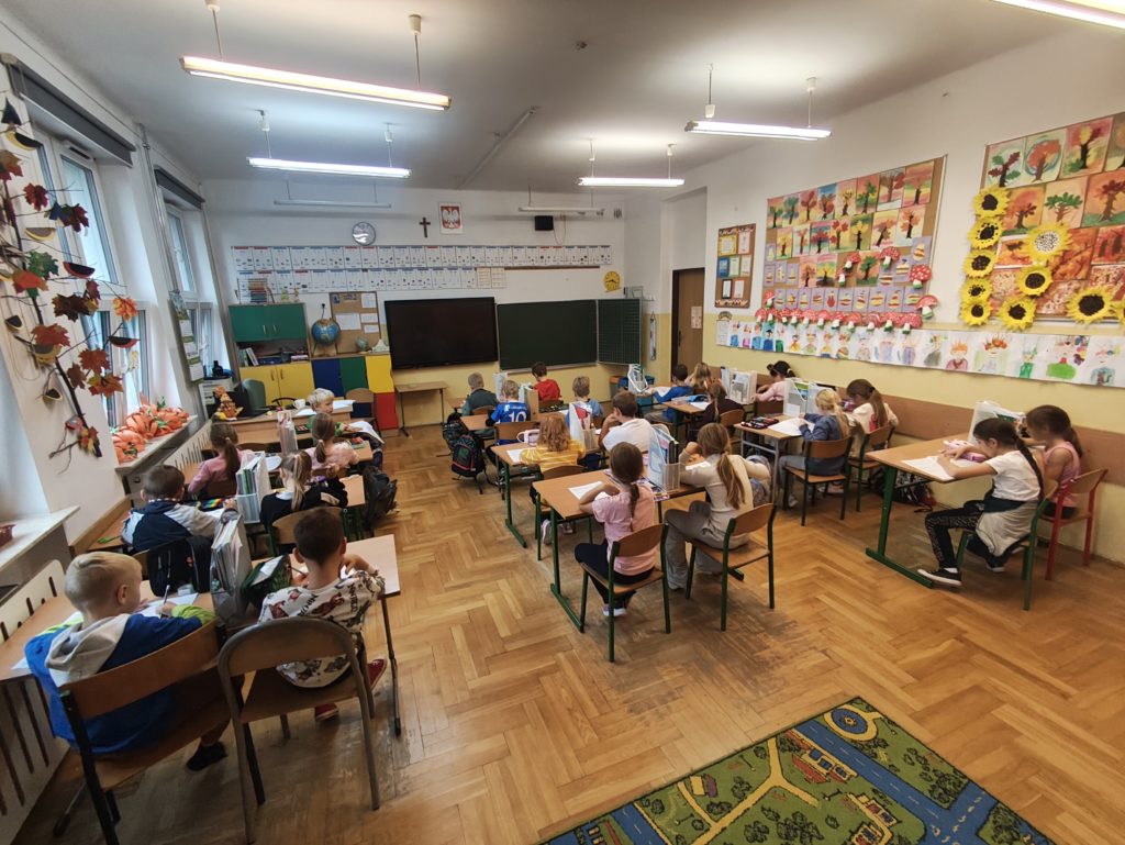 W sali maluchów siedzą uczniowie i piszą pracę pisemną. Na zdjęciu są plecy uczniów, z przodu sali jest tablica.